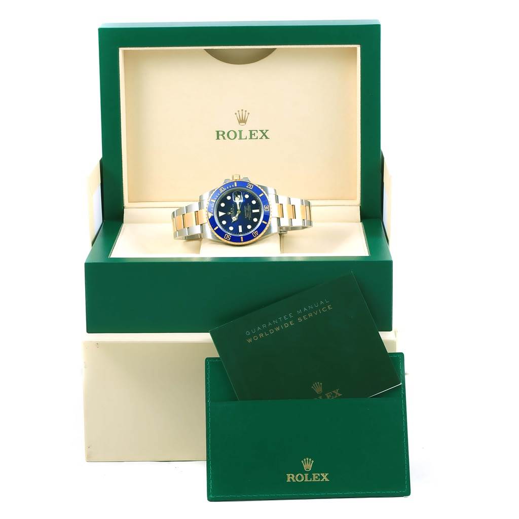 The image shows a Rolex Submariner 116613 Men's Steel and Gold (two tone) Blue Dial 116613 Men's Steel and Gold (two tone) Blue Dial watch in a green box with service manuals placed in front.