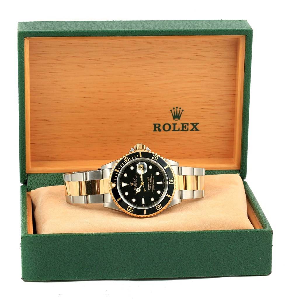 The Rolex Submariner 16613 Men
s Steel and Gold (two tone) Black Dial 16613 Men
s Steel and Gold (two tone) Black Dial watch is displayed front-on in an open green and wooden Rolex box.
