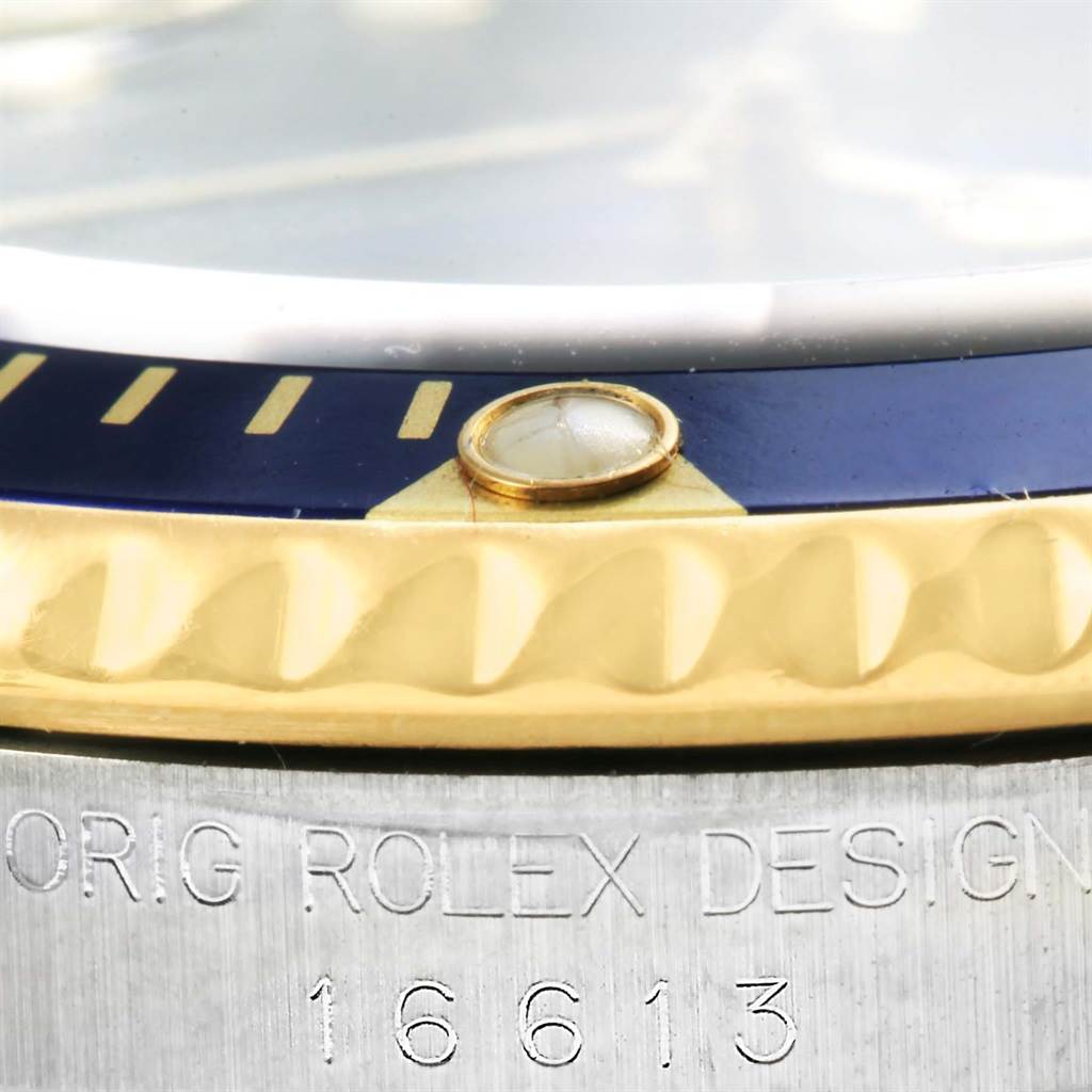 This close-up image of the Rolex Submariner 16613 Men's Steel and Gold (two tone) Blue Dial 16613 Men's Steel and Gold (two tone) Blue Dial model shows its bezel, lume pip, and part of the model number engraving.