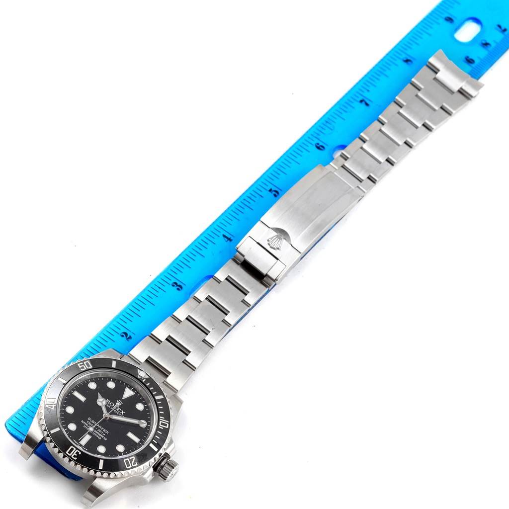 The Rolex Submariner 114060 Men's Stainless Steel Black Dial 114060 Men's Stainless Steel Black Dial watch is shown from a top view with its stainless steel bracelet laid out next to a ruler.