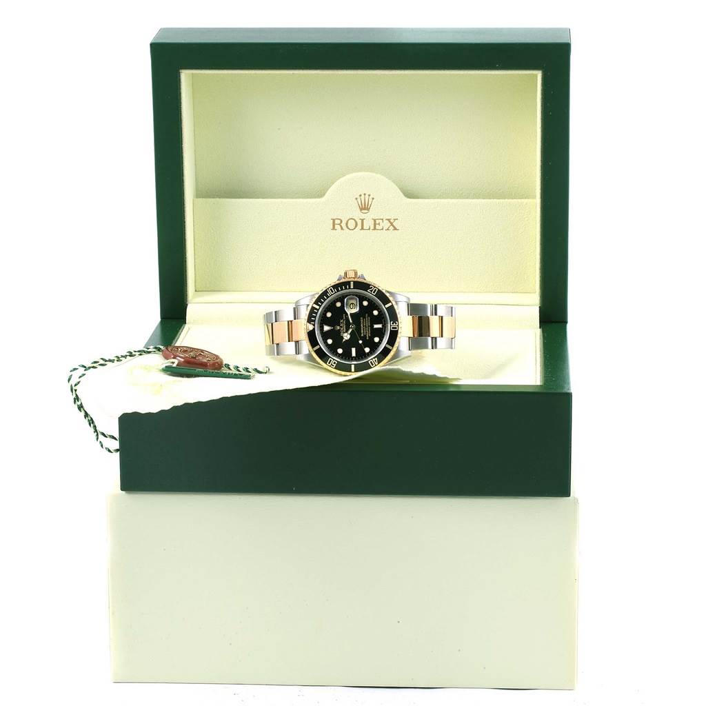 The Rolex Submariner 16613 Men
s Steel and Gold (two tone) Black Dial 16613 Men
s Steel and Gold (two tone) Black Dial watch is shown front-on in an open green and cream box, with the brand logo visible in the background.
