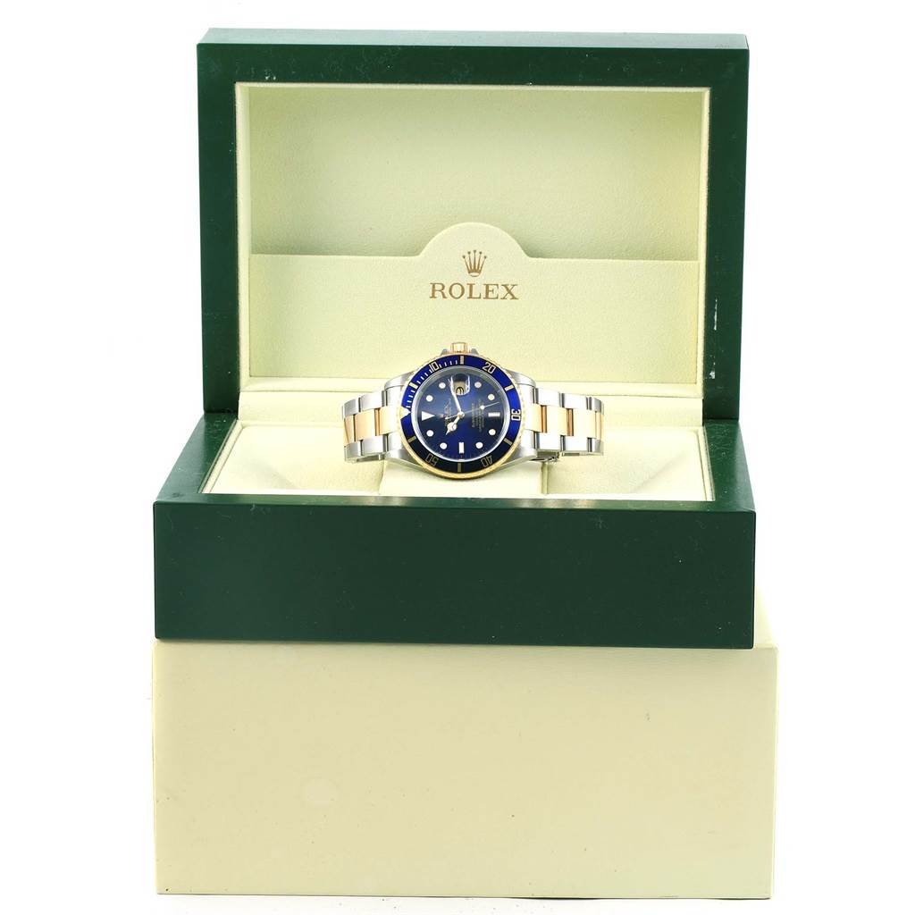The Rolex Submariner 16613 Men's Steel and Gold (two tone) Blue Dial 16613 Men's Steel and Gold (two tone) Blue Dial watch is displayed inside its open green and beige box, showing the face and bracelet.