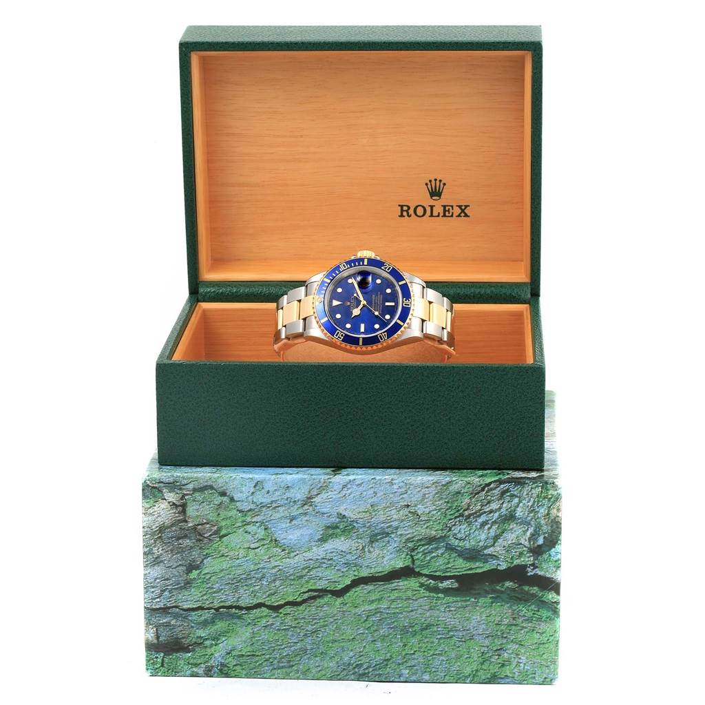 The Rolex Submariner 16613 Men's Steel and Gold (two tone) Blue Dial 16613 Men's Steel and Gold (two tone) Blue Dial watch is shown face-up inside its open green and wooden box.
