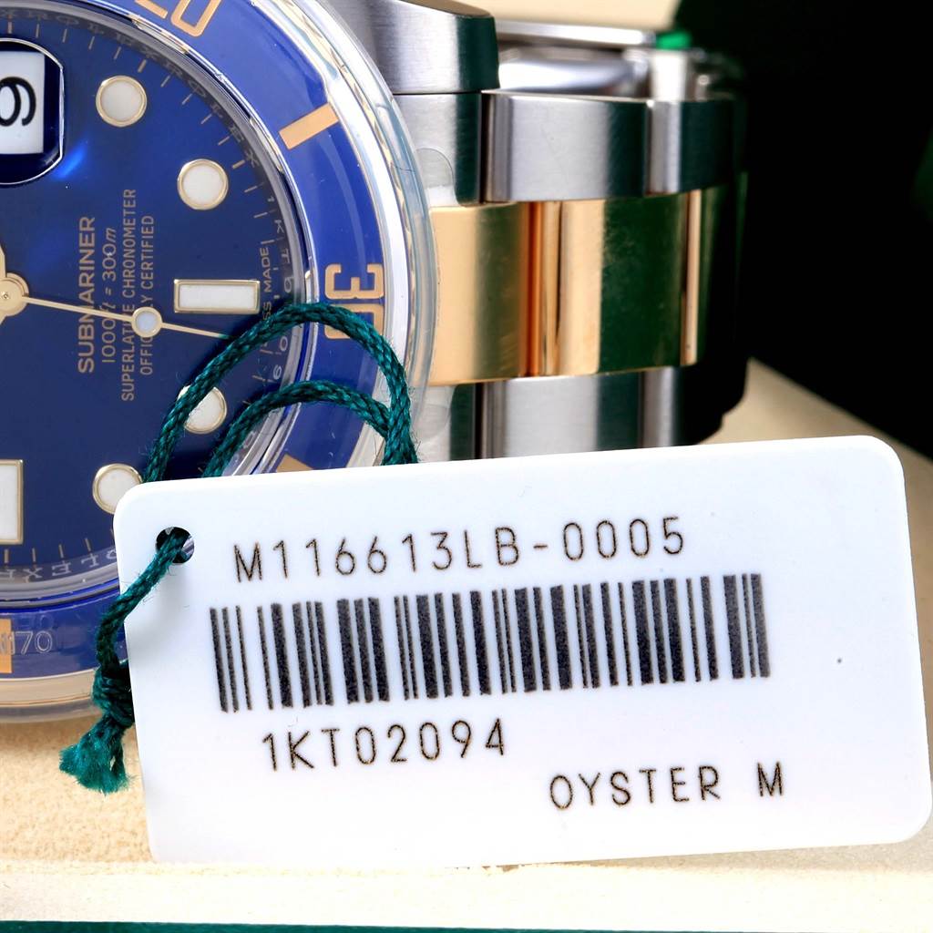 The image shows a close-up of a Rolex Submariner 116613 Men's Steel and Gold (two tone) Blue Dial 116613 Men's Steel and Gold (two tone) Blue Dial’s face, blue dial, and bi-metal band, along with a tag displaying the model number.