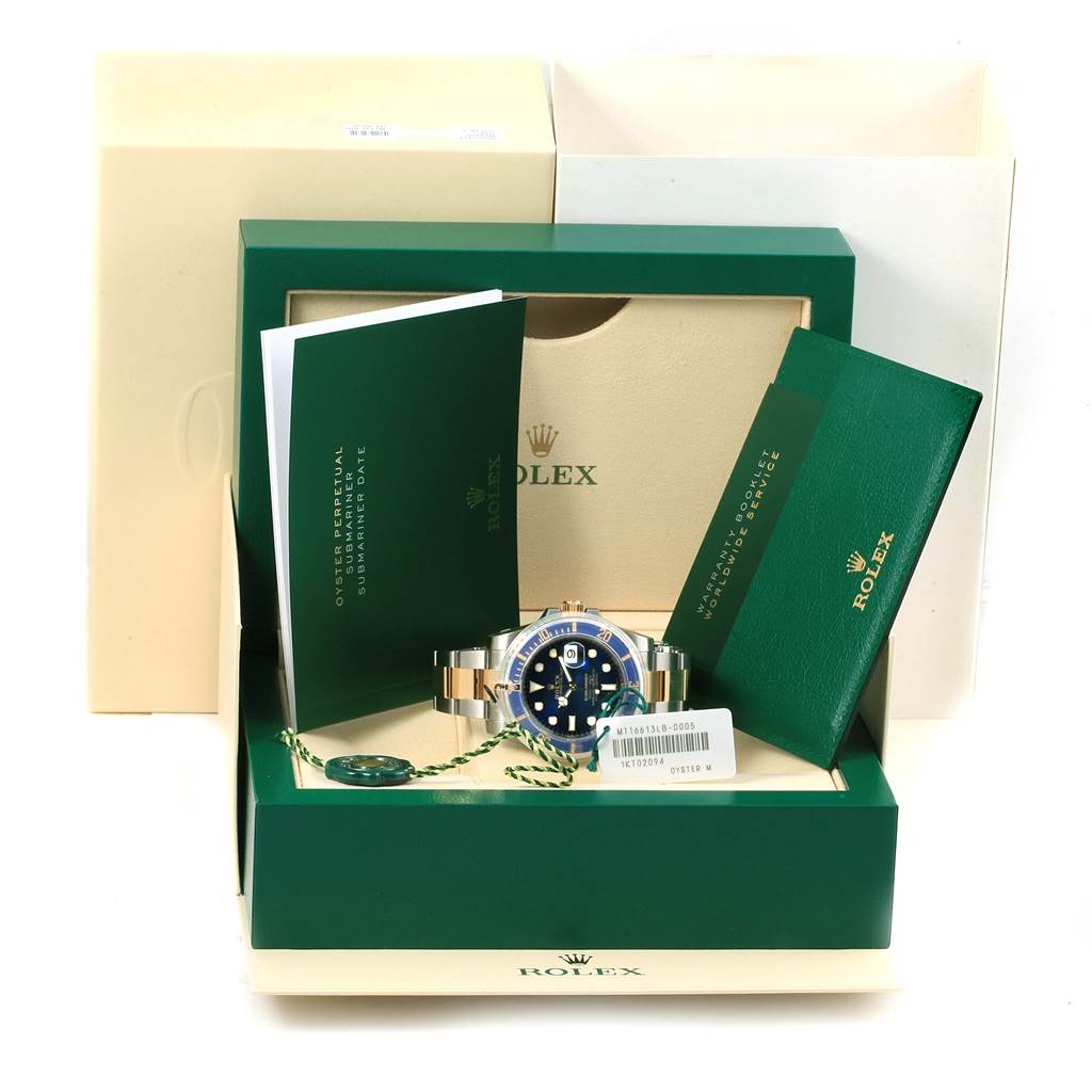 The image shows a Rolex Submariner 116613 Men's Steel and Gold (two tone) Blue Dial 116613 Men's Steel and Gold (two tone) Blue Dial watch in its packaging, with manuals, tag, and warranty card visible.
