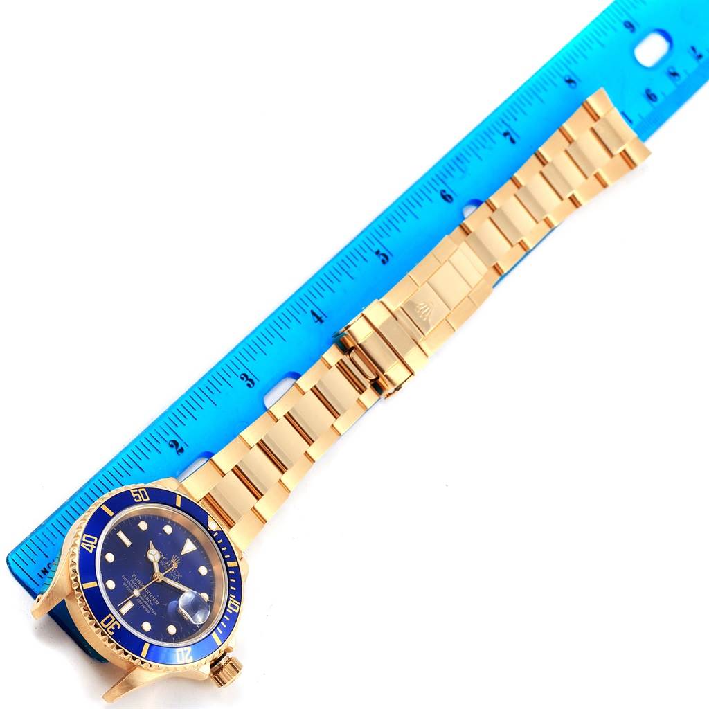 The image shows the dial, bezel, and bracelet of a Rolex Submariner 16618 Men's Yellow Gold Blue Dial 16618 Men's Yellow Gold Blue Dial, laid flat next to a blue ruler.