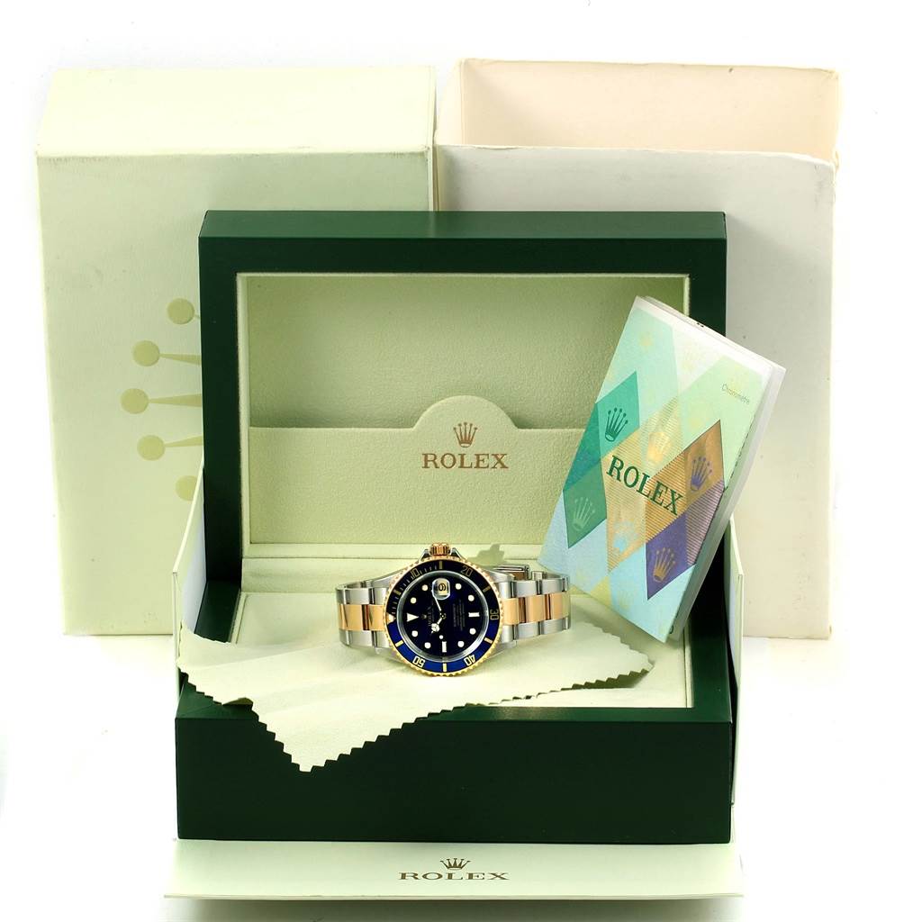 The image shows a Rolex Submariner 16613 Men's Steel and Gold (two tone) Blue Dial 16613 Men's Steel and Gold (two tone) Blue Dial watch in its open box with documentation and a cleaning cloth.