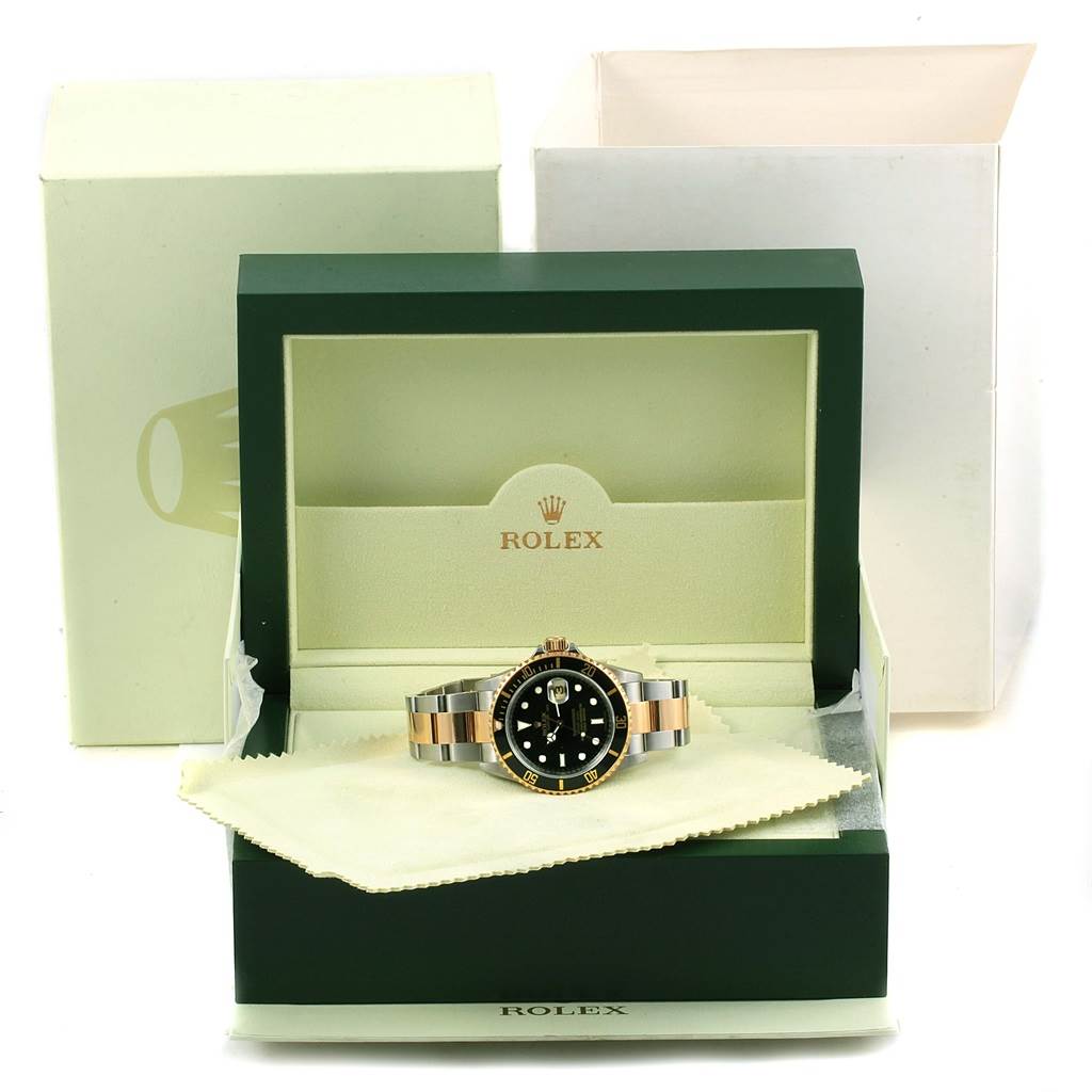 The image shows a Rolex Submariner 16613 Men
s Steel and Gold (two tone) Black Dial 16613 Men
s Steel and Gold (two tone) Black Dial watch from a front angle, placed inside an open Rolex box with packaging in the background.