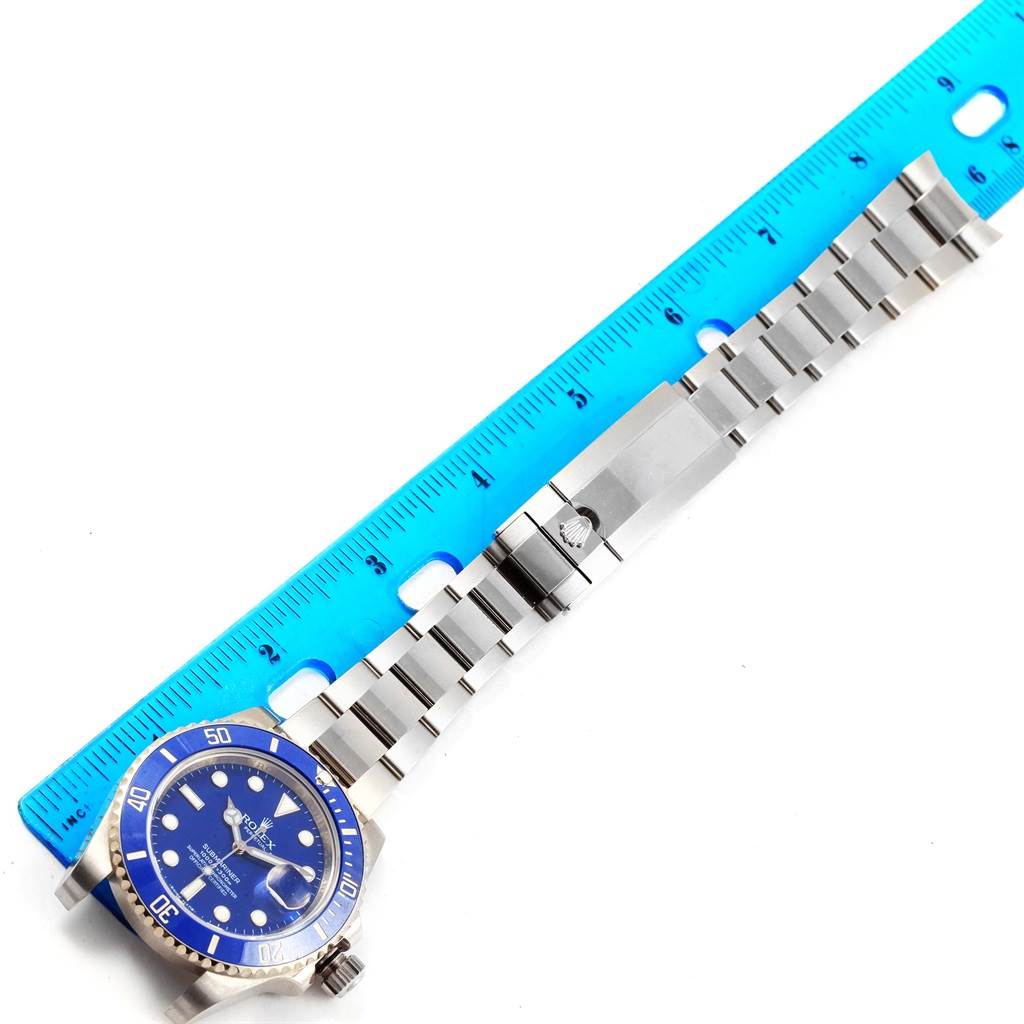 The image shows a Rolex Submariner 116619 Men's White Gold Blue Dial 116619 Men's White Gold Blue Dial watch with a blue dial and stainless steel bracelet, alongside a blue ruler for scale.