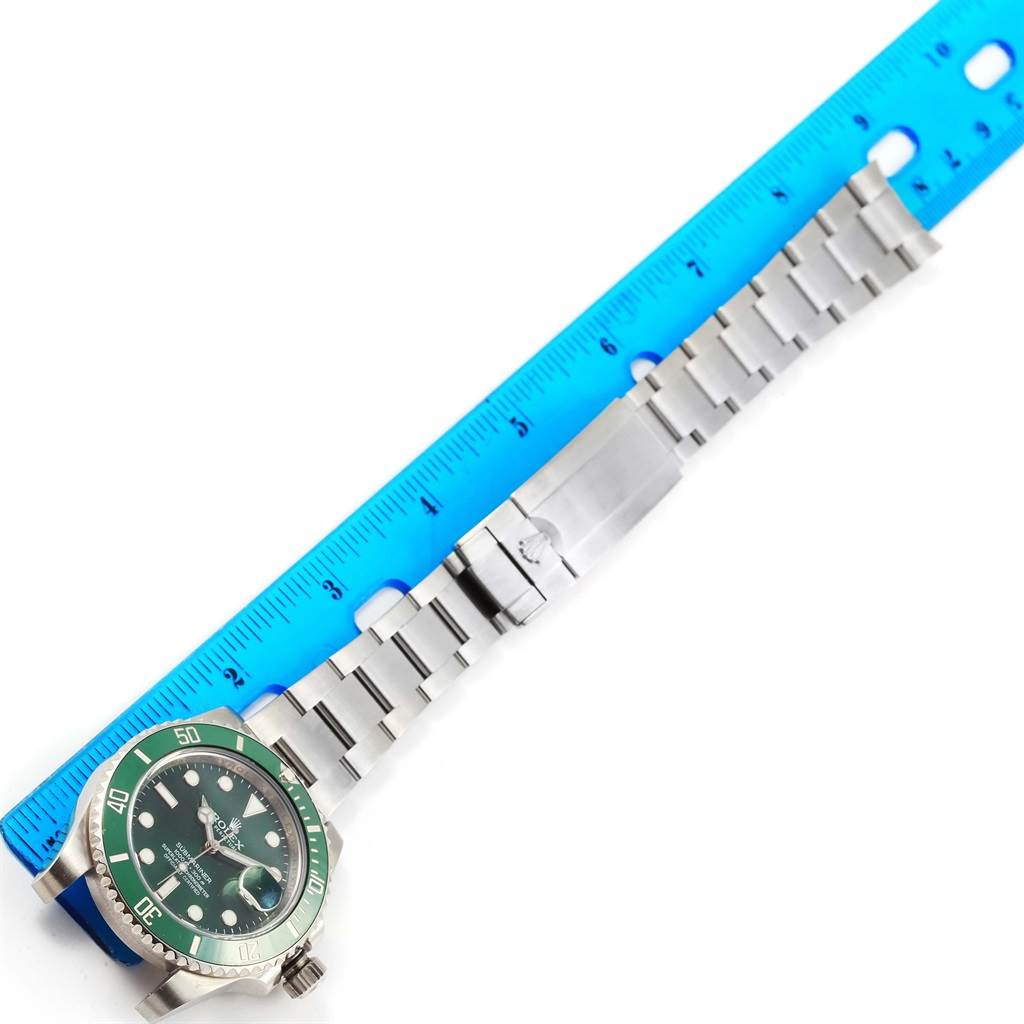 The image shows a side view of a Rolex Submariner 116610LV Men
s Stainless Steel Green Dial 116610LV Men
s Stainless Steel Green Dial watch and its bracelet laid alongside a blue ruler for scale.