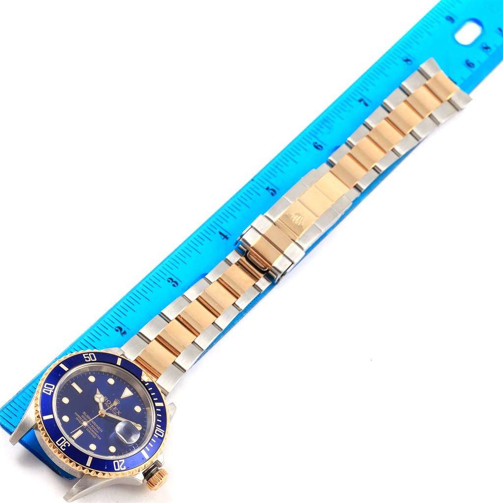 The image shows a side and top view of the Rolex Submariner 16613 Men's Steel and Gold (two tone) Blue Dial 16613 Men's Steel and Gold (two tone) Blue Dial, featuring its blue dial, bezel, and metal bracelet next to a ruler.
