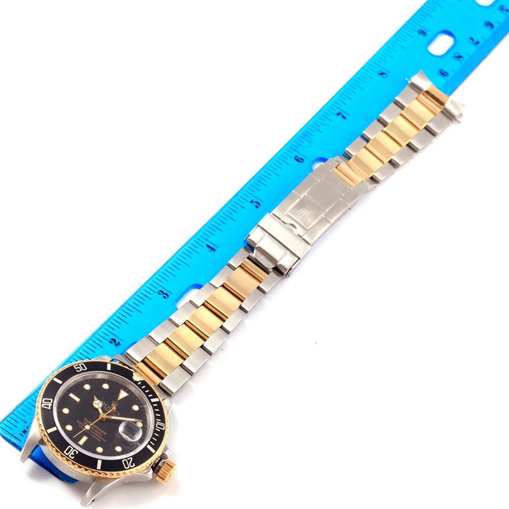 The image shows a top-down view of a Rolex Submariner 16803 Men's Steel and Gold (two tone) Black Dial 16803 Men's Steel and Gold (two tone) Black Dial watch, focusing on the face and stainless steel and gold bracelet, measured against a ruler.