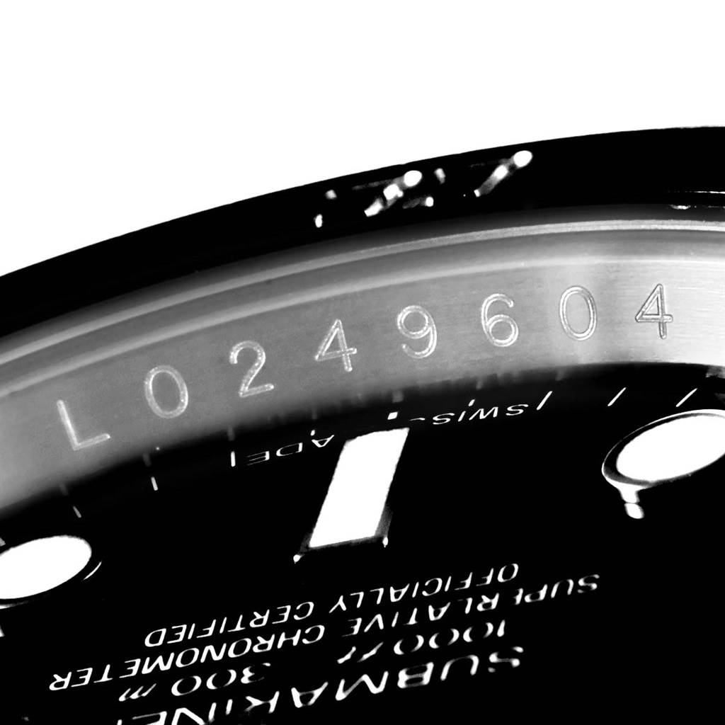 This image shows a close-up of the serial number engraved on the case and part of the dial of a Rolex Submariner 114060 Men's Stainless Steel Black Dial 114060 Men's Stainless Steel Black Dial watch.