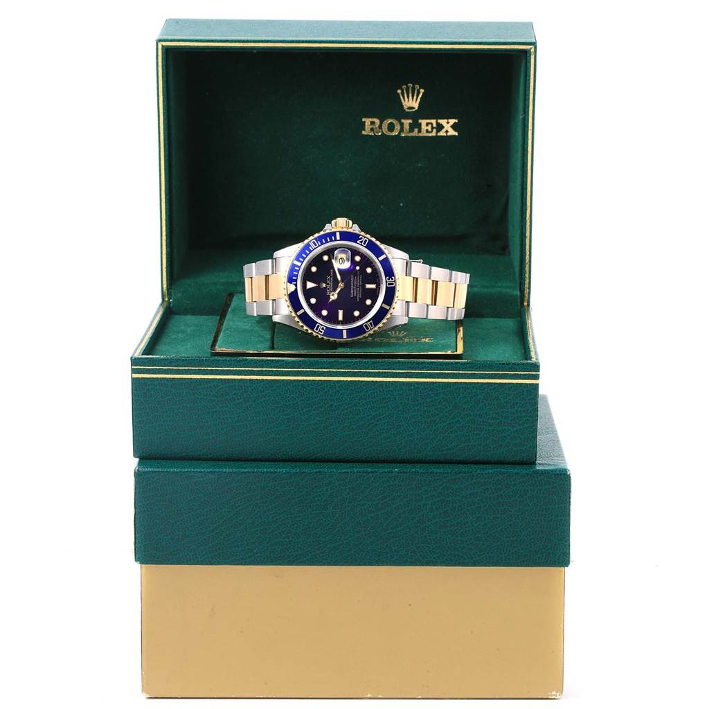 The Rolex Submariner 16613 Men
s Steel and Gold (two tone) Purple Dial 16613 Men
s Steel and Gold (two tone) Purple Dial watch is shown front-facing inside an open green box with a gold interior and logo.