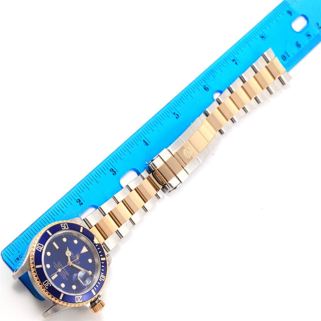 The Rolex Submariner 16613 Men's Steel and Gold (two tone) Blue Dial 16613 Men's Steel and Gold (two tone) Blue Dial watch is displayed with its blue and gold dial, bezel, and bracelet, measured next to a blue ruler.