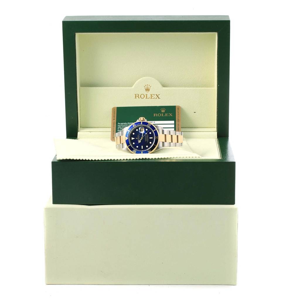 The image shows a Rolex Submariner 16613 Men's Steel and Gold (two tone) Blue Dial 16613 Men's Steel and Gold (two tone) Blue Dial watch with a blue dial and gold bracelet inside a Rolex box with its guarantee card.