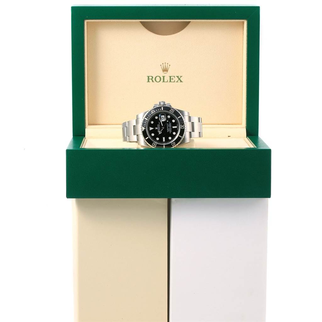 The Rolex Submariner 116610 Men's Stainless Steel Black Dial 116610 Men's Stainless Steel Black Dial watch is displayed frontally inside its opened green and beige branded box.