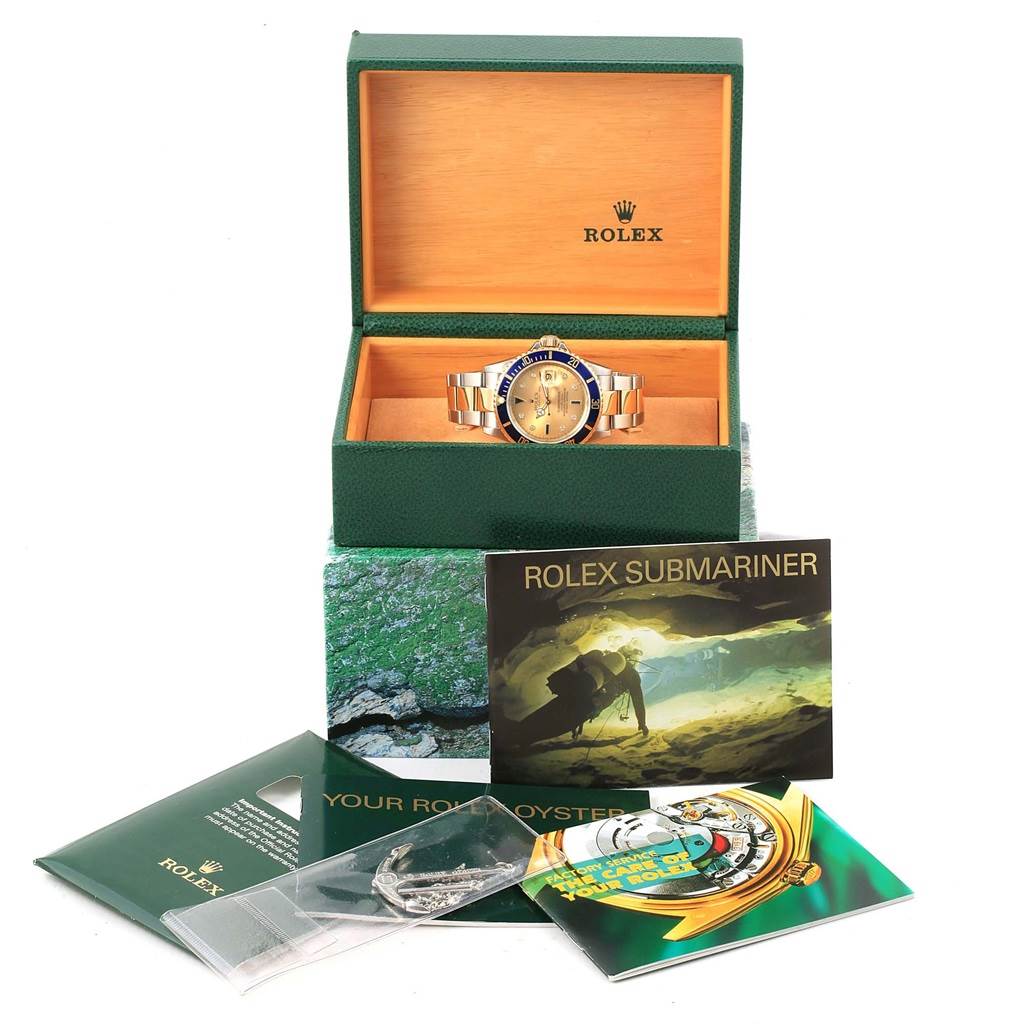 The image shows a Rolex Submariner 16613 Men's Steel and Gold (two tone) Champagne Dial 16613 Men's Steel and Gold (two tone) Champagne Dial watch in a green box with accompanying booklets and accessories.