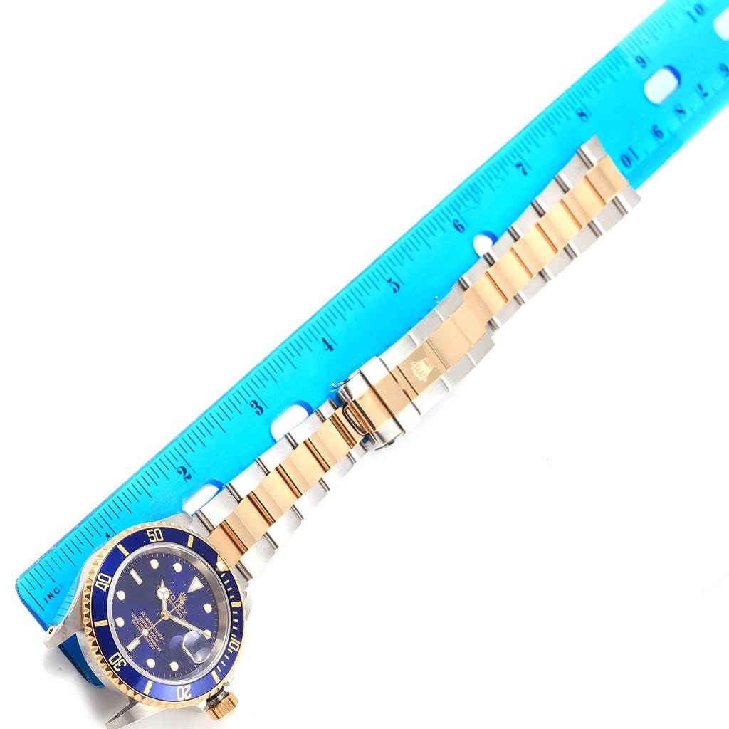 The image shows a top-down view of a Rolex Submariner 16613 Men's Steel and Gold (two tone) Blue Dial 16613 Men's Steel and Gold (two tone) Blue Dial watch with a two-tone bracelet next to a blue ruler.