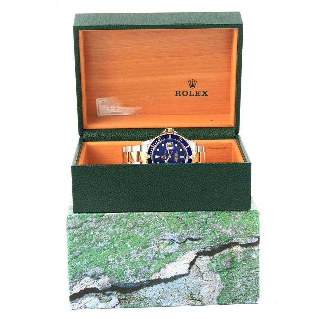The image shows a Rolex Submariner 16613 Men's Steel and Gold (two tone) Blue Dial 16613 Men's Steel and Gold (two tone) Blue Dial watch, partially visible, displayed in an open green and wooden box.
