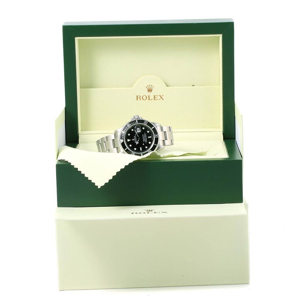 The Rolex Submariner 16610 Men's Stainless Steel Black Dial 16610 Men's Stainless Steel Black Dial watch is shown at an angle inside its open green and cream presentation box.