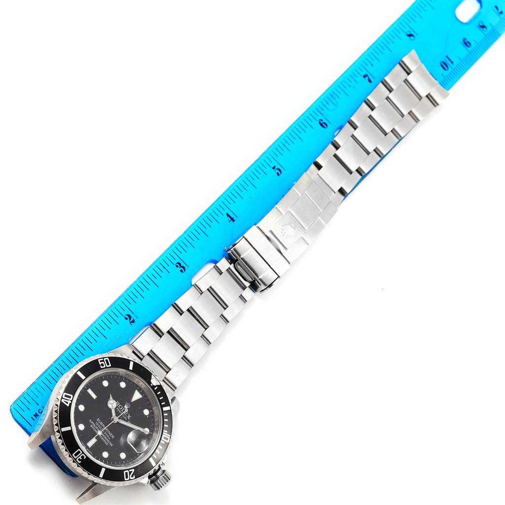 The Rolex Submariner 16610 Men's Stainless Steel Black Dial 16610 Men's Stainless Steel Black Dial watch is shown flat with its face and entire stainless steel bracelet visible, next to a blue ruler for scale.