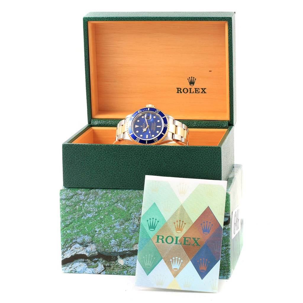 The image shows a Rolex Submariner 16613 Men's Steel and Gold (two tone) Blue Dial 16613 Men's Steel and Gold (two tone) Blue Dial watch placed in an open Rolex box with a booklet in front of the box.