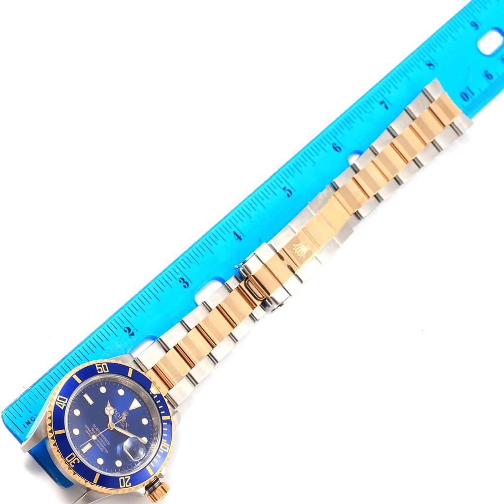 The image shows a Rolex Submariner 16613 Men's Steel and Gold (two tone) Blue Dial 16613 Men's Steel and Gold (two tone) Blue Dial watch laid flat next to a ruler, displaying the watch face and band.