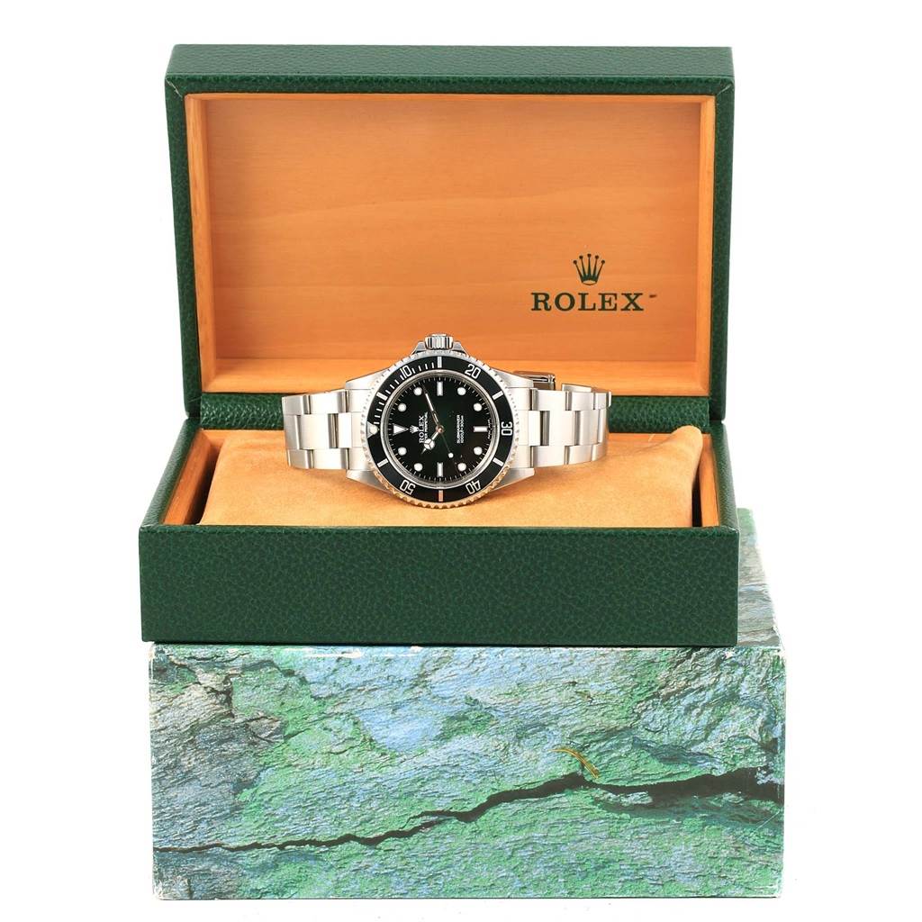 The Rolex Submariner 14060 Men's Stainless Steel Black Dial 14060 Men's Stainless Steel Black Dial watch is displayed front-on, in an open green Rolex box, resting on an orange cushion.