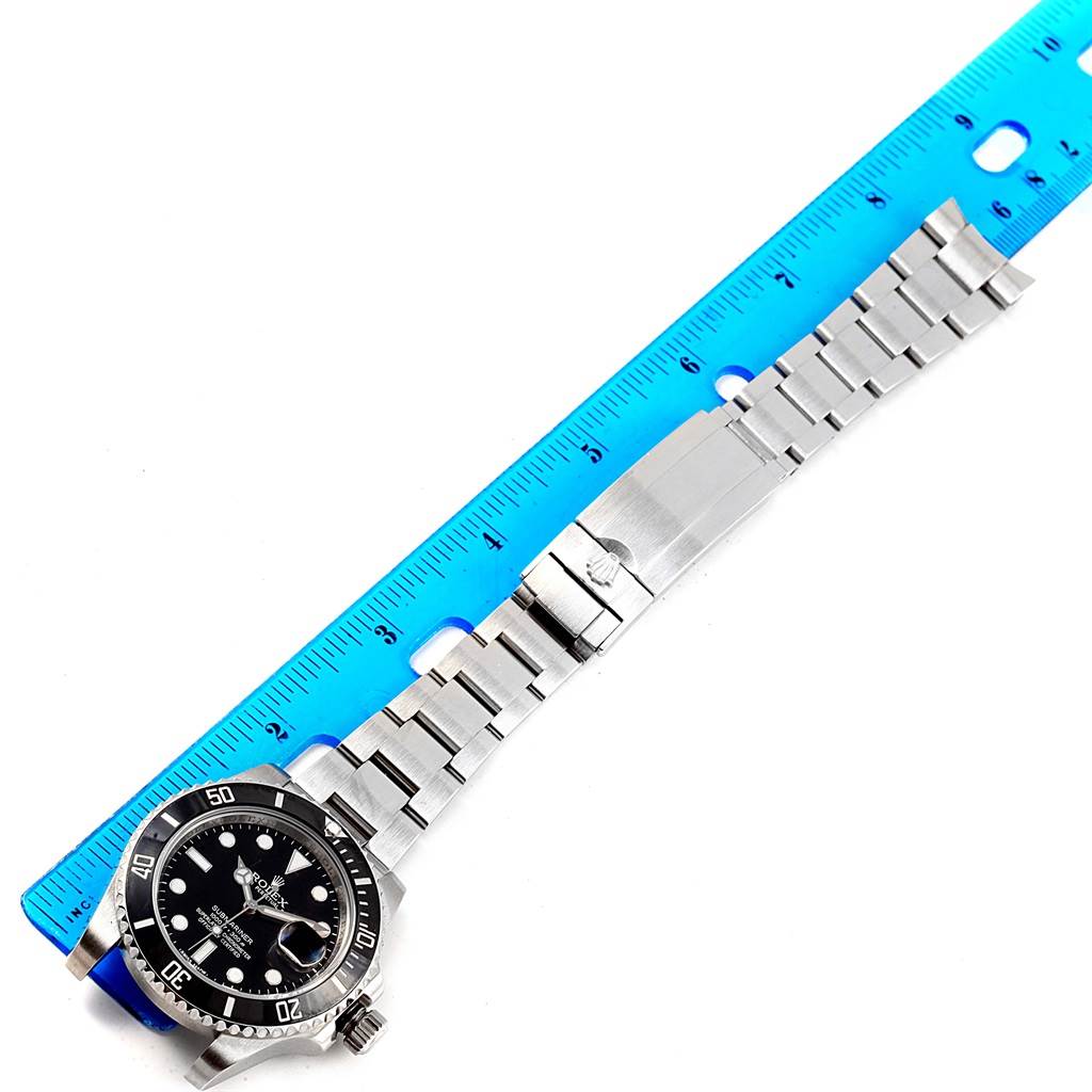 The image shows a Rolex Submariner 116610 Men's Stainless Steel Black Dial 116610 Men's Stainless Steel Black Dial watch laid flat with a blue ruler for scale, displaying the face and metal band.