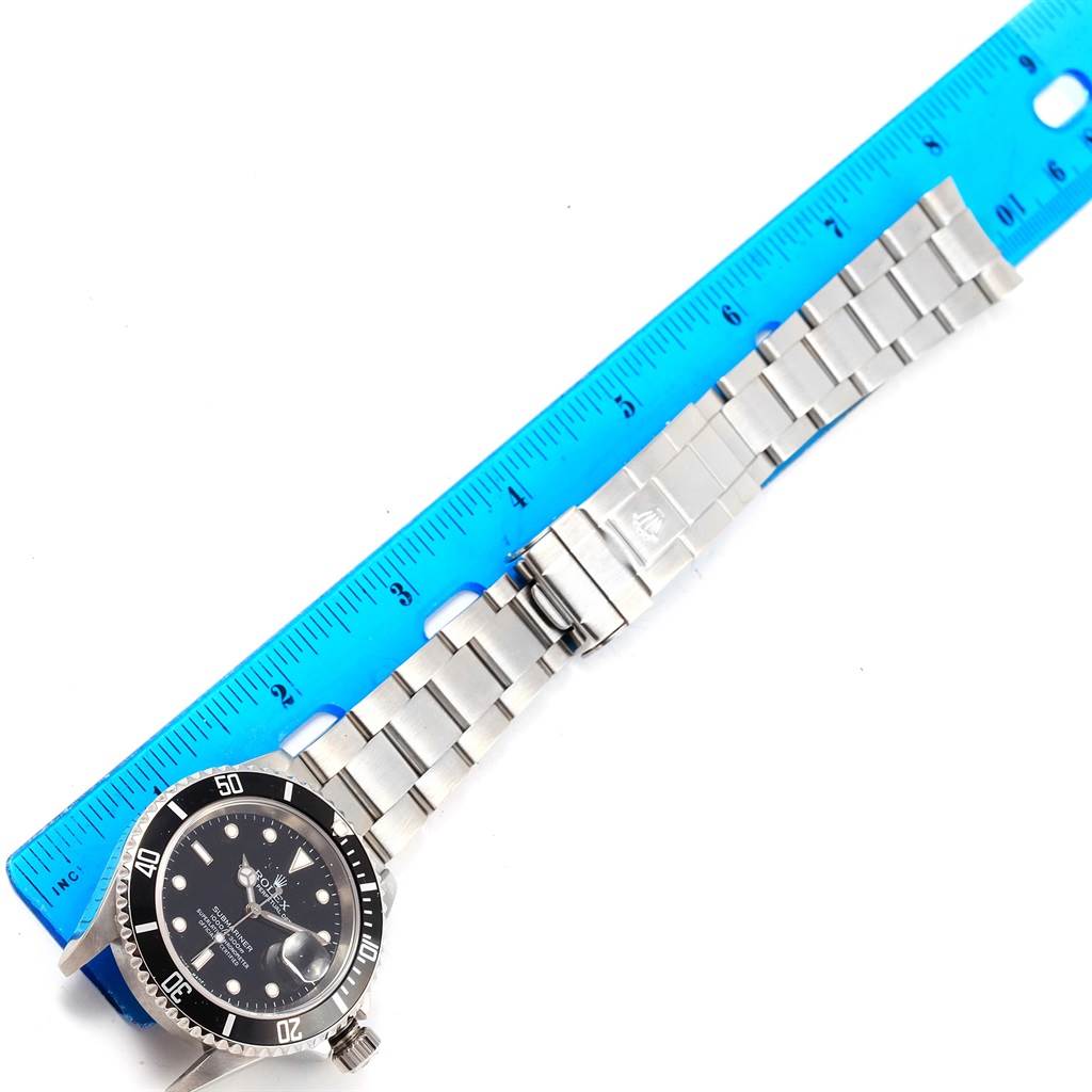 The Rolex Submariner 16610 Men's Stainless Steel Black Dial 16610 Men's Stainless Steel Black Dial watch is shown laid flat with its bracelet extended next to a ruler for scale.