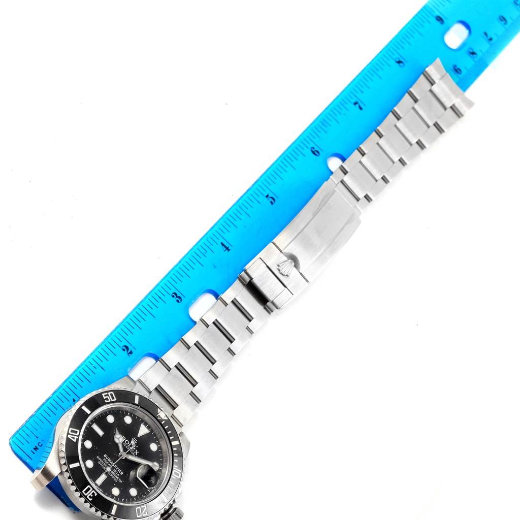 The image shows a top view of a Rolex Submariner 116610 Men's Stainless Steel Black Dial 116610 Men's Stainless Steel Black Dial watch, including its face, bezel, and metal bracelet alongside a blue ruler.