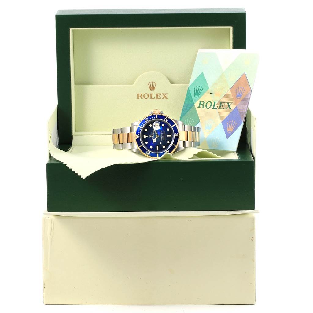 The Rolex Submariner 16613 Men's Steel and Gold (two tone) Blue Dial 16613 Men's Steel and Gold (two tone) Blue Dial watch is displayed front-facing in an open box, alongside authentication paperwork.