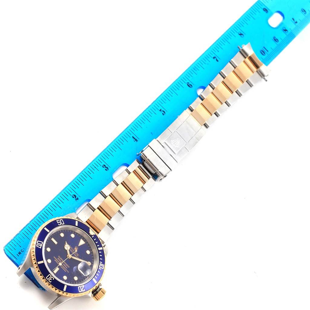The image shows a Rolex Submariner 16613 Men's Steel and Gold (two tone) Blue Dial 16613 Men's Steel and Gold (two tone) Blue Dial watch and its bracelet, including the case, bezel, and clasp, with a ruler alongside for measurement.