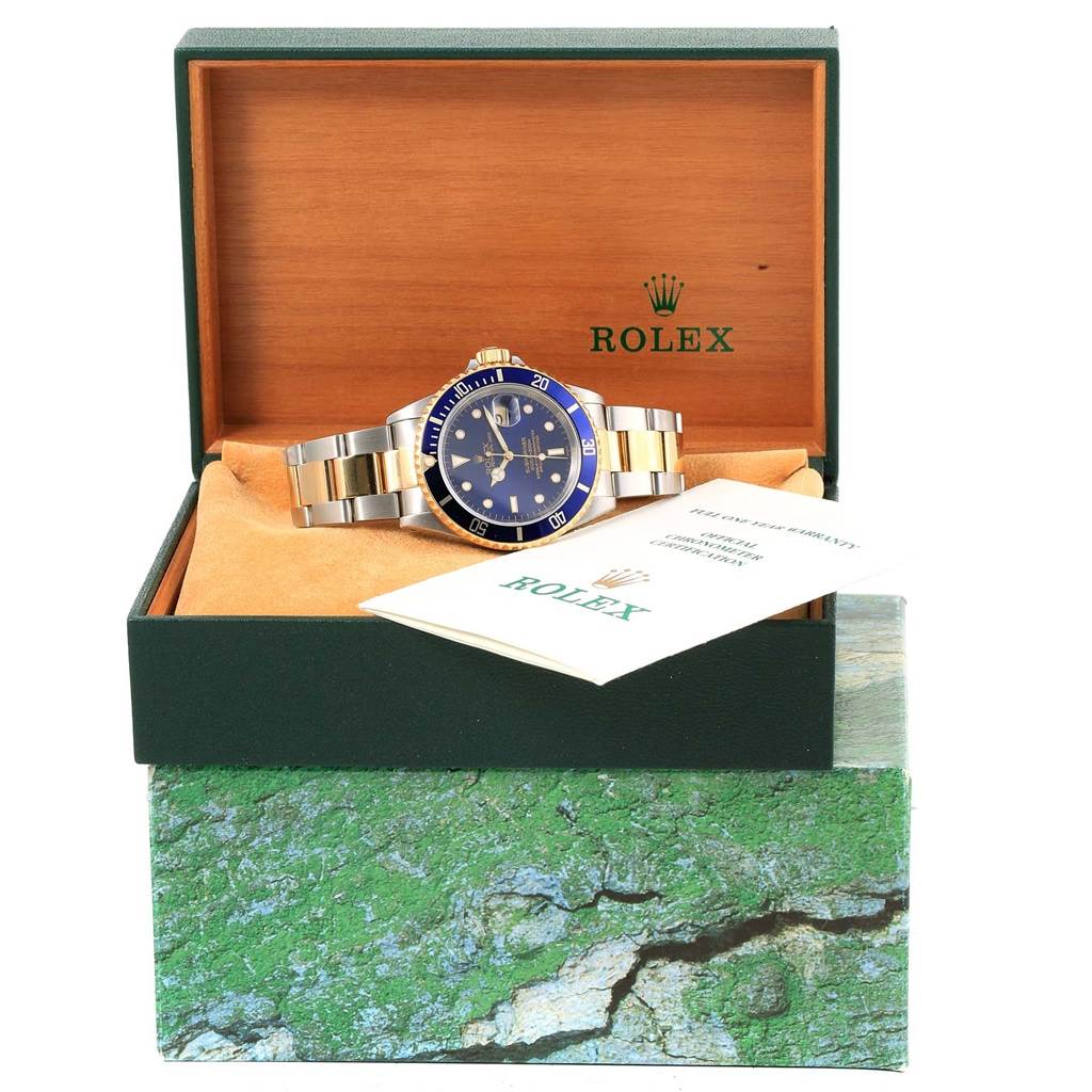 The Rolex Submariner 16613 Men's Steel and Gold (two tone) Blue Dial 16613 Men's Steel and Gold (two tone) Blue Dial watch is displayed in its box, with a view of the face, bracelet, and accompanying paperwork.