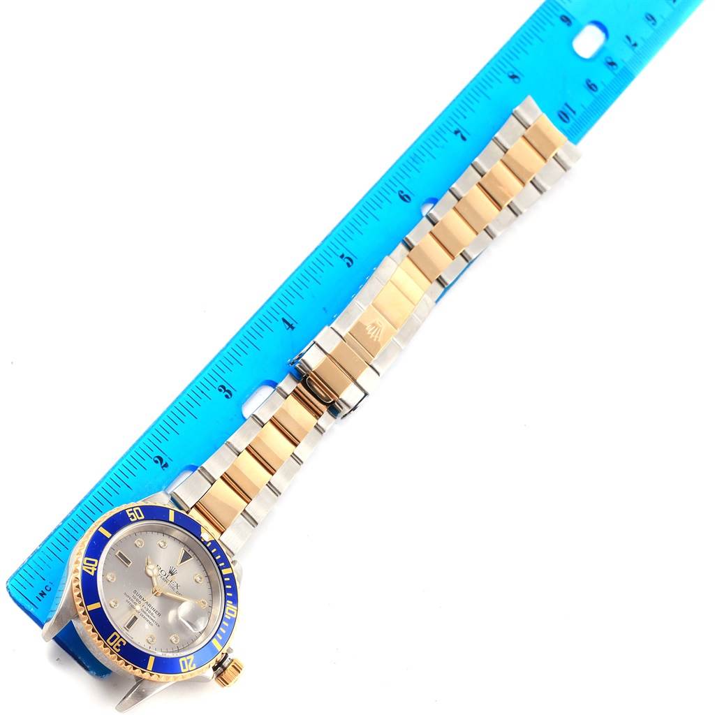 The Rolex Submariner 16613 Men's Steel and Gold (two tone) Grey Dial 16613 Men's Steel and Gold (two tone) Grey Dial watch is shown from a top-down angle with its bezel, dial, bracelet, and a blue ruler for scale.