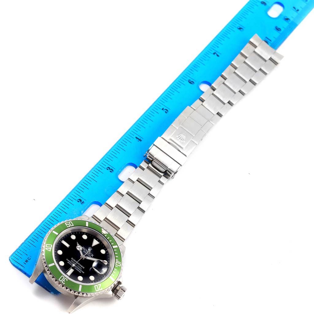 The image shows the front view of a Rolex Submariner 16610LV Men's Stainless Steel Black Dial 16610LV Men's Stainless Steel Black Dial watch with a green bezel and stainless steel bracelet, placed next to a ruler.