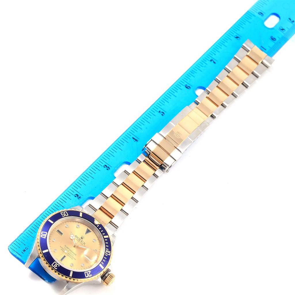 A Rolex Submariner 16613 Men's Steel and Gold (two tone) Champagne Dial 16613 Men's Steel and Gold (two tone) Champagne Dial watch is displayed flat with its bracelet aligned next to a ruler for measurement.