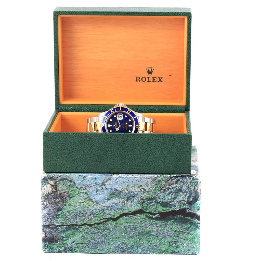 The image shows a Rolex Submariner 16613 Men's Steel and Gold (two tone) Blue Dial 16613 Men's Steel and Gold (two tone) Blue Dial watch from the front, partially inside an open green and wood-colored Rolex box.