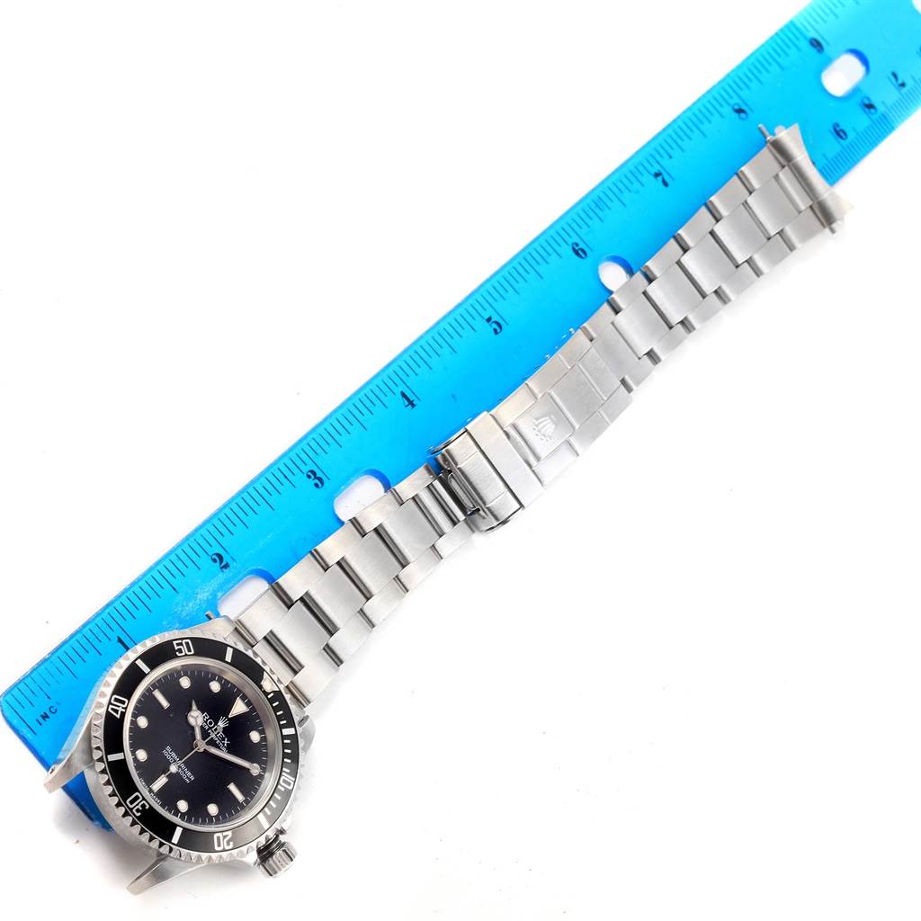 The Rolex Submariner 14060 Men's Stainless Steel Black Dial 14060 Men's Stainless Steel Black Dial watch is shown lying flat, with its stainless steel bracelet extended next to a blue ruler.