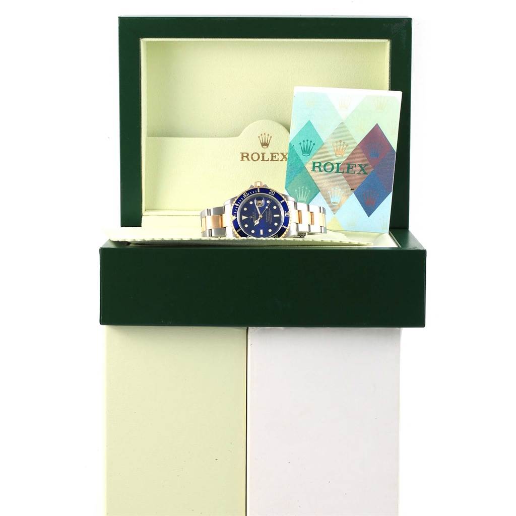 This image shows a Rolex Submariner 16613 Men's Steel and Gold (two tone) Blue Dial 16613 Men's Steel and Gold (two tone) Blue Dial watch displayed in an open green box with its brand card placed next to it.