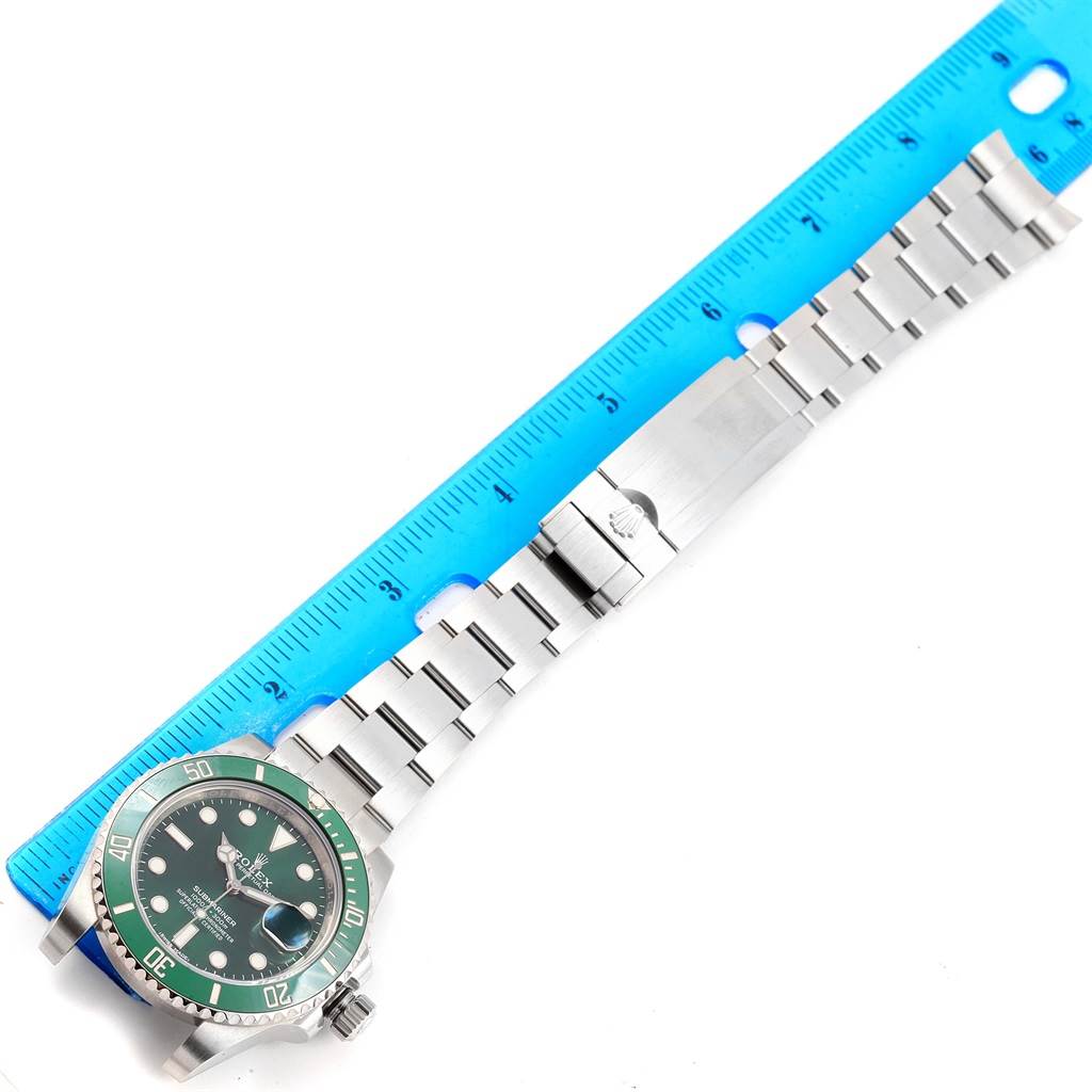 The image shows a Rolex Submariner 116610LV Men's Stainless Steel Green Dial 116610LV Men's Stainless Steel Green Dial watch with its stainless steel bracelet aligned alongside a blue ruler.