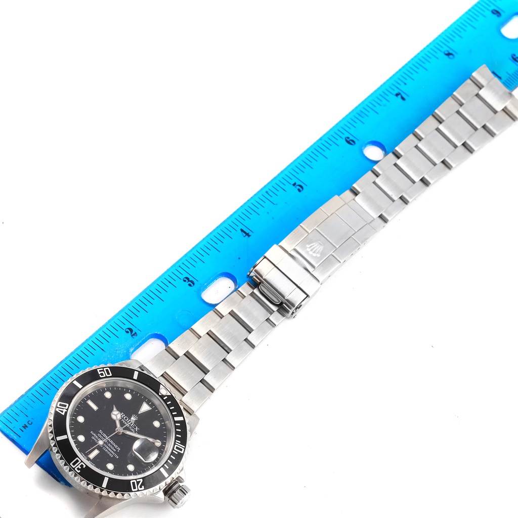 This image shows the face, bezel, and metal bracelet of a Rolex Submariner 16610 Men's Stainless Steel Black Dial 16610 Men's Stainless Steel Black Dial watch, measured against a blue ruler.