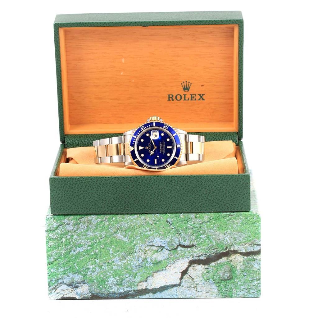 The image shows a front view of a Rolex Submariner 16613 Men's Steel and Gold (two tone) Blue Dial 16613 Men's Steel and Gold (two tone) Blue Dial watch with a blue dial, displayed in its open green and wooden box.