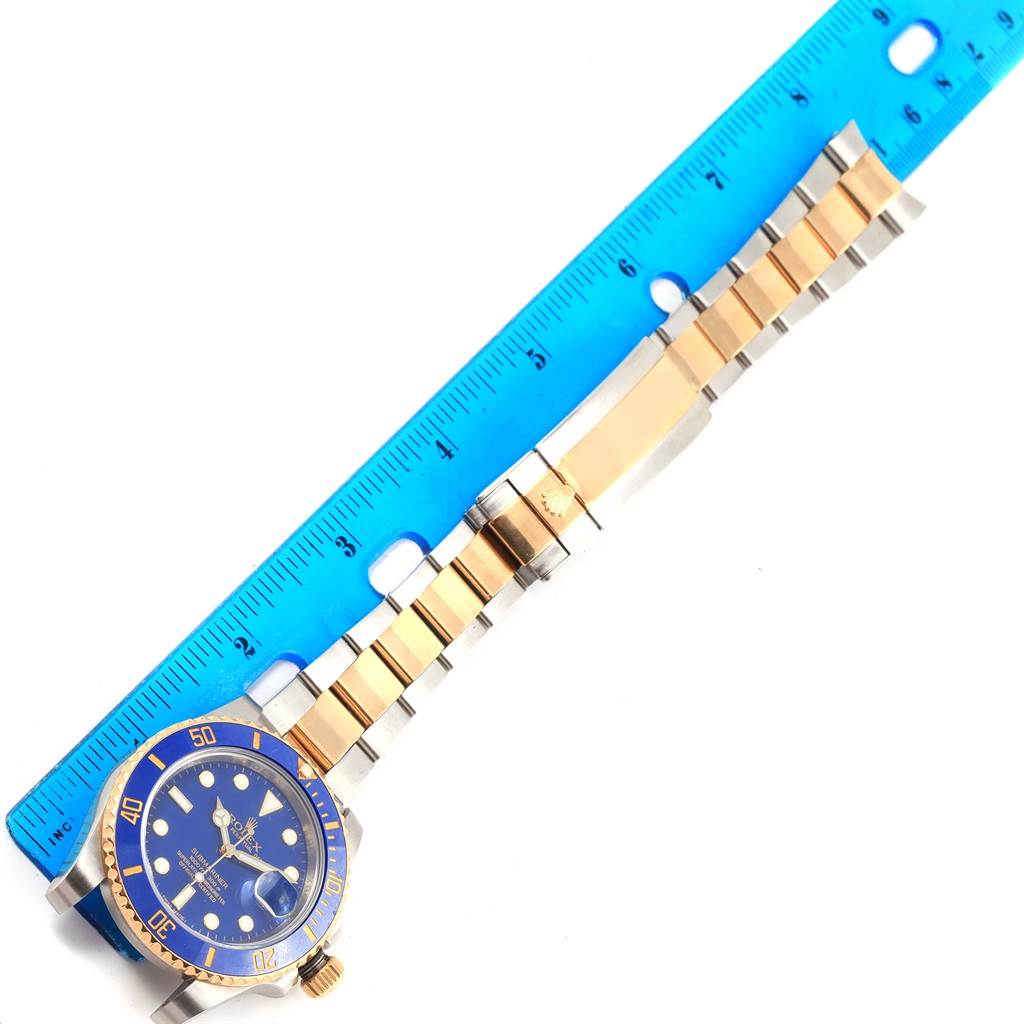 The Rolex Submariner 116613 Men's Steel and Gold (two tone) Blue Dial 116613 Men's Steel and Gold (two tone) Blue Dial watch is shown laid flat with its blue and gold bracelet measured by a blue ruler.