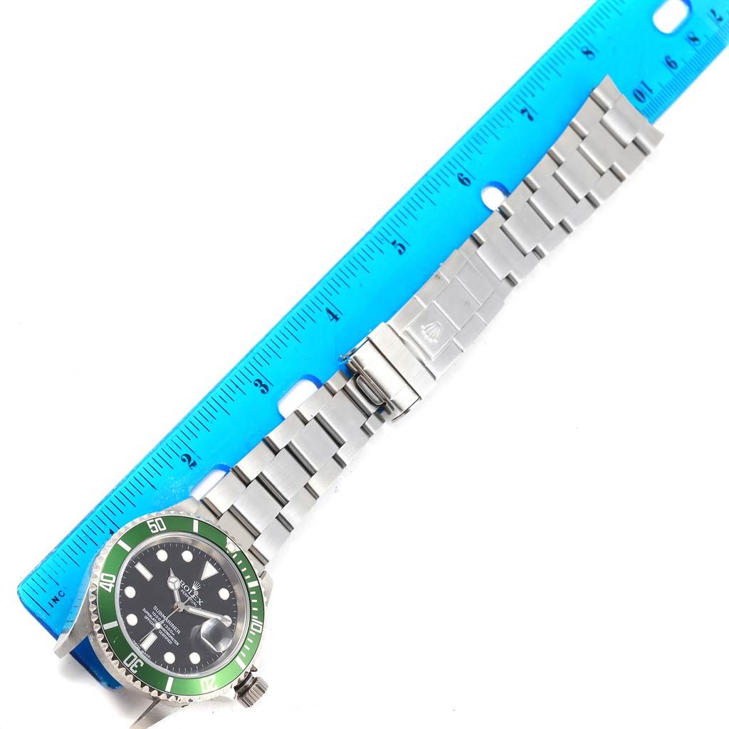 The image shows a Rolex Submariner 16610LV Men's Stainless Steel Black Dial 16610LV Men's Stainless Steel Black Dial watch laid flat with its stainless steel bracelet and clasp, alongside a blue ruler.