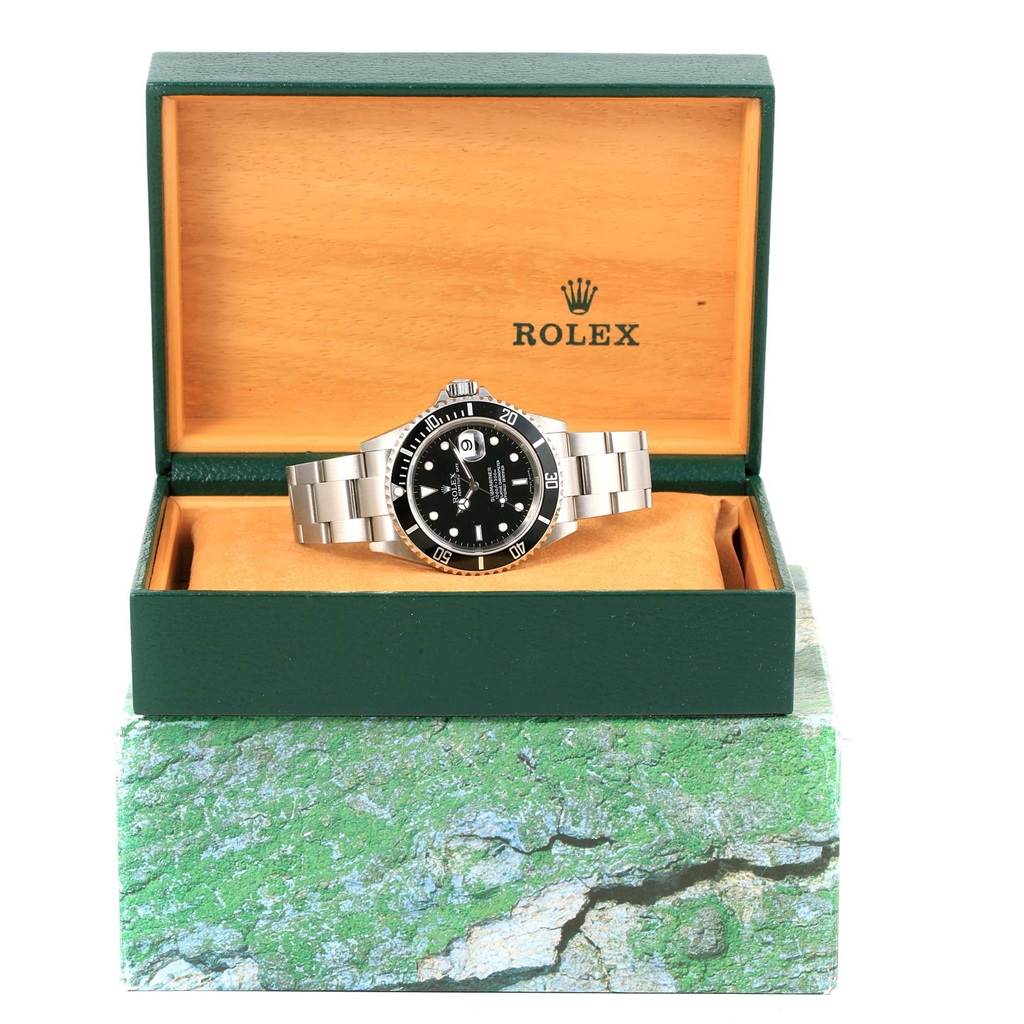 The Rolex Submariner 16610 Men's Stainless Steel Black Dial 16610 Men's Stainless Steel Black Dial watch is shown front-on inside its open green and wooden case.