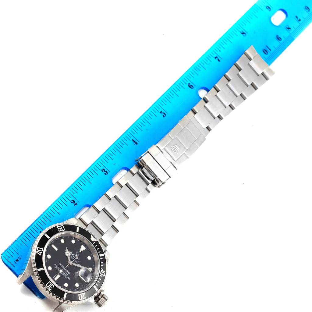 The image shows a Rolex Submariner 16610 Men's Stainless Steel Black Dial 16610 Men's Stainless Steel Black Dial watch from an overhead angle, displaying its face, bezel, and metal bracelet beside a ruler.