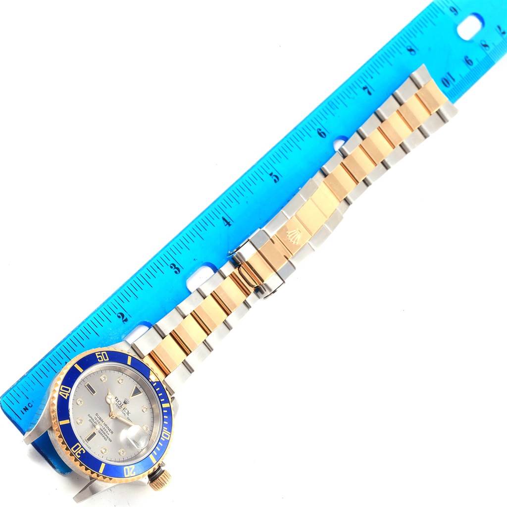 The image shows a Rolex Submariner 16613 Men's Steel and Gold (two tone) Grey Dial 16613 Men's Steel and Gold (two tone) Grey Dial watch from the top view, highlighting the bezel, dial, and the two-tone bracelet alongside a ruler.
