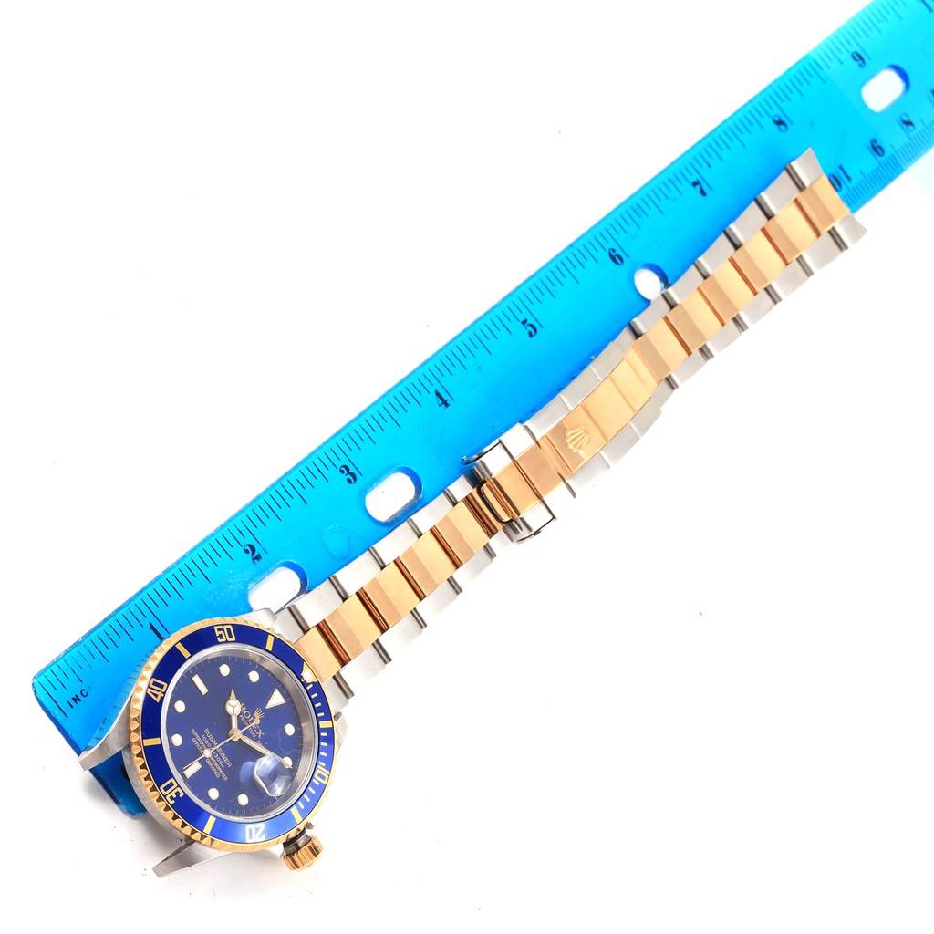 The image shows a Rolex Submariner 16613 Men's Steel and Gold (two tone) Blue Dial 16613 Men's Steel and Gold (two tone) Blue Dial watch laid flat, measured next to a ruler, highlighting the watch face and metal band.